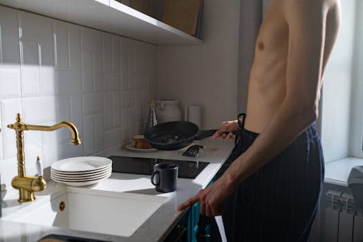 A young man prepares breakfast in a sunlit kitchen, capturing a daily routine moment.