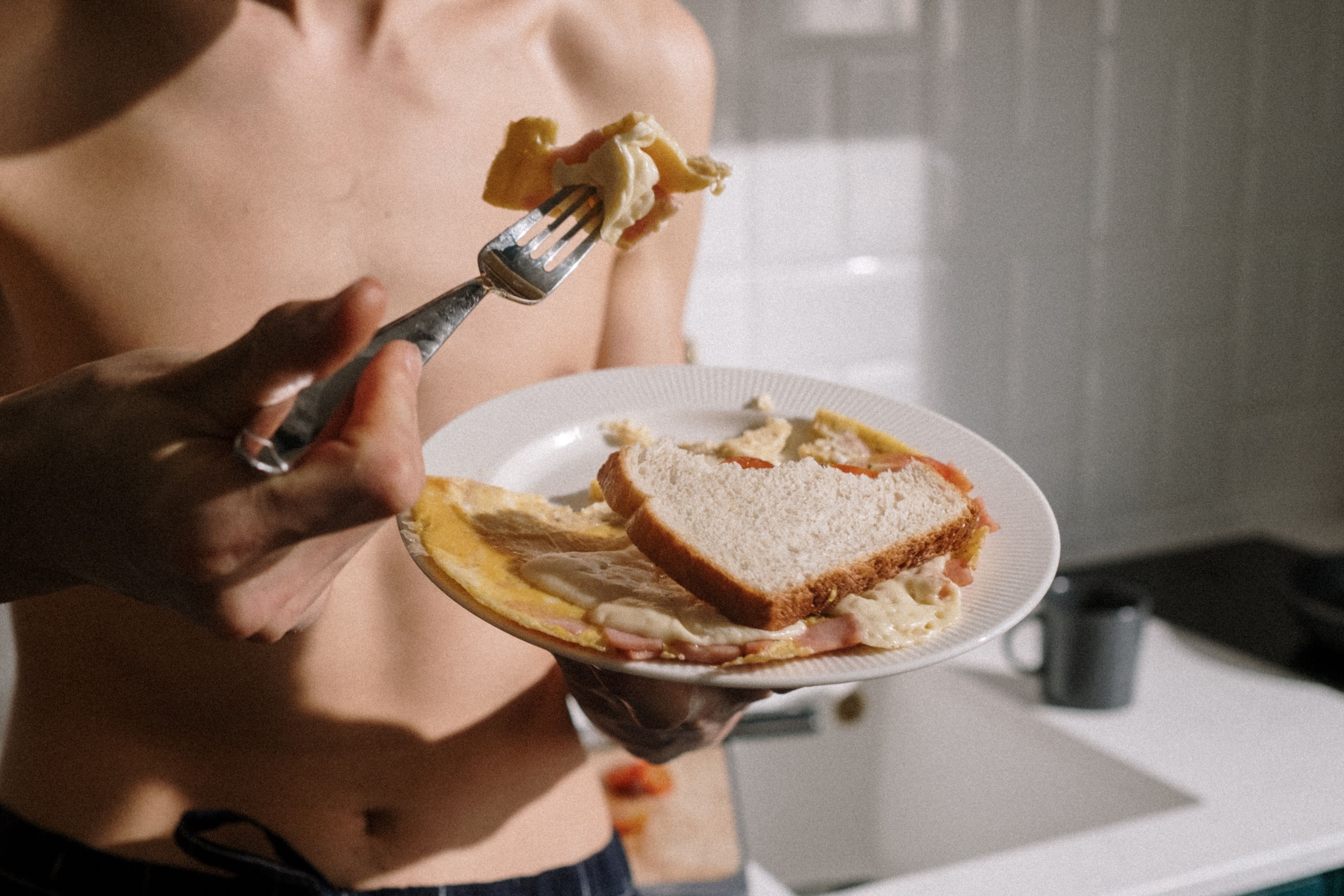 Man standing in kitchen, eating omelette with toast. Morning meal indoors.