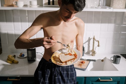 Free Topless Man in Blue and White Plaid Shorts Holding Stainless Steel Fork and Knife Slicing Cake Stock Photo