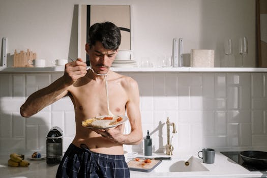 Young man enjoying a breakfast omelette in a sunlit kitchen setting.