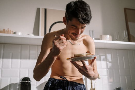 Smiling young man eats breakfast in a bright kitchen, enjoying a sunny morning.