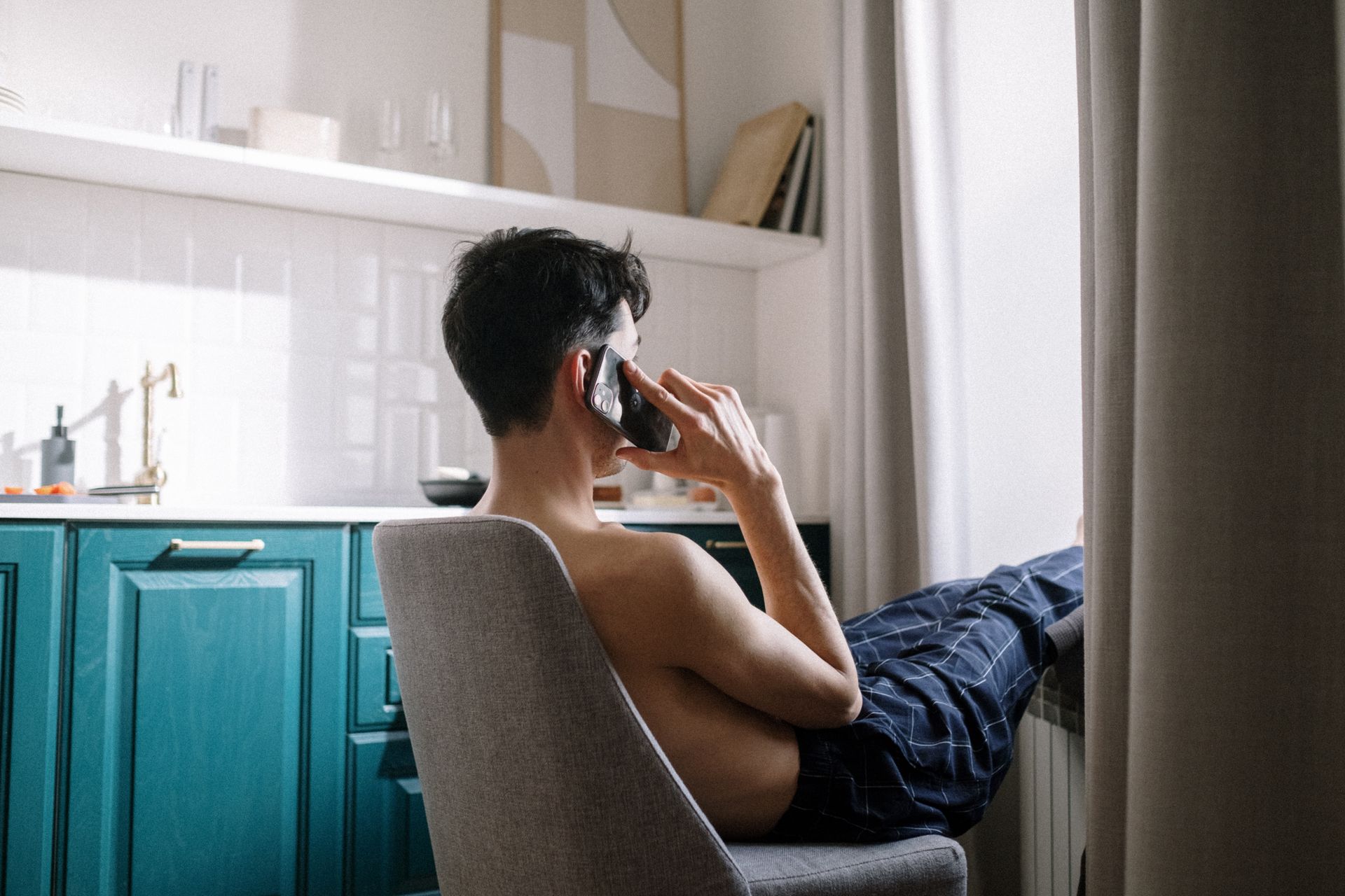 Man lounging by the window, talking on the phone in a modern room.