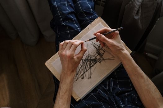 A person drawing abstract lines on paper, focusing on hands and pencil, indoors.