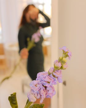 A blurred artistic photo featuring a woman holding delicate purple stock flowers indoors.