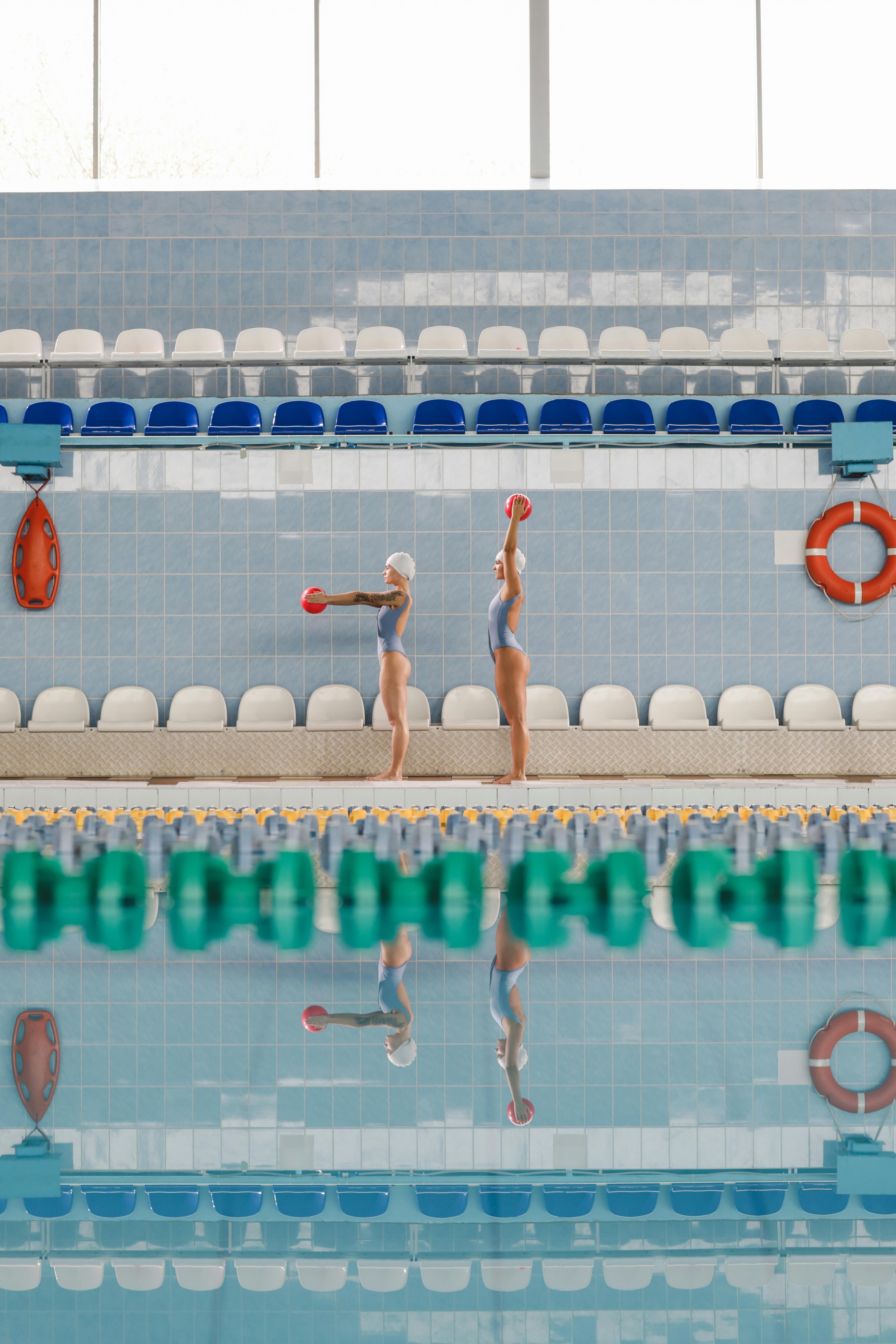 women in bikini standing on pool ledge holding red balls