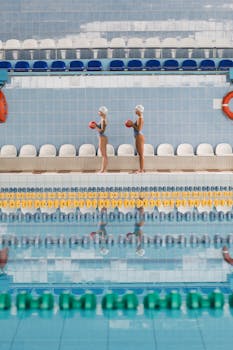 Two female swimmers practicing synchronized swimming in an indoor pool.
