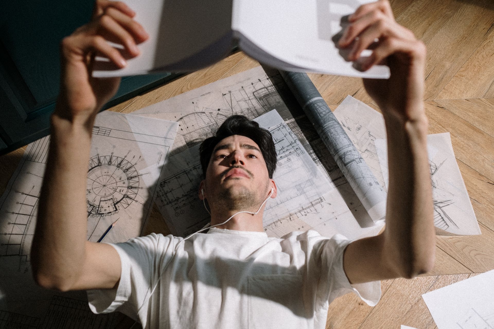 Young architect in white t-shirt examines blueprints indoors, focused and dedicated.