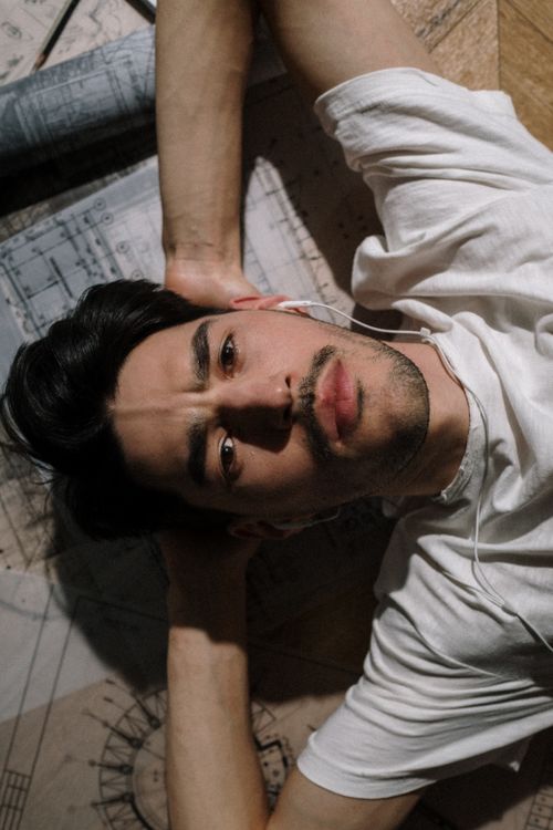 Free Portrait of a man lying indoors on blueprints, listening to music with earphones. Stock Photo