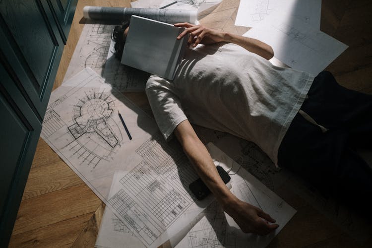 Man Laying Down On Floor With Notebook On Face