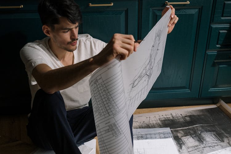 Adult Man Sitting On Floor And Looking At Drawing