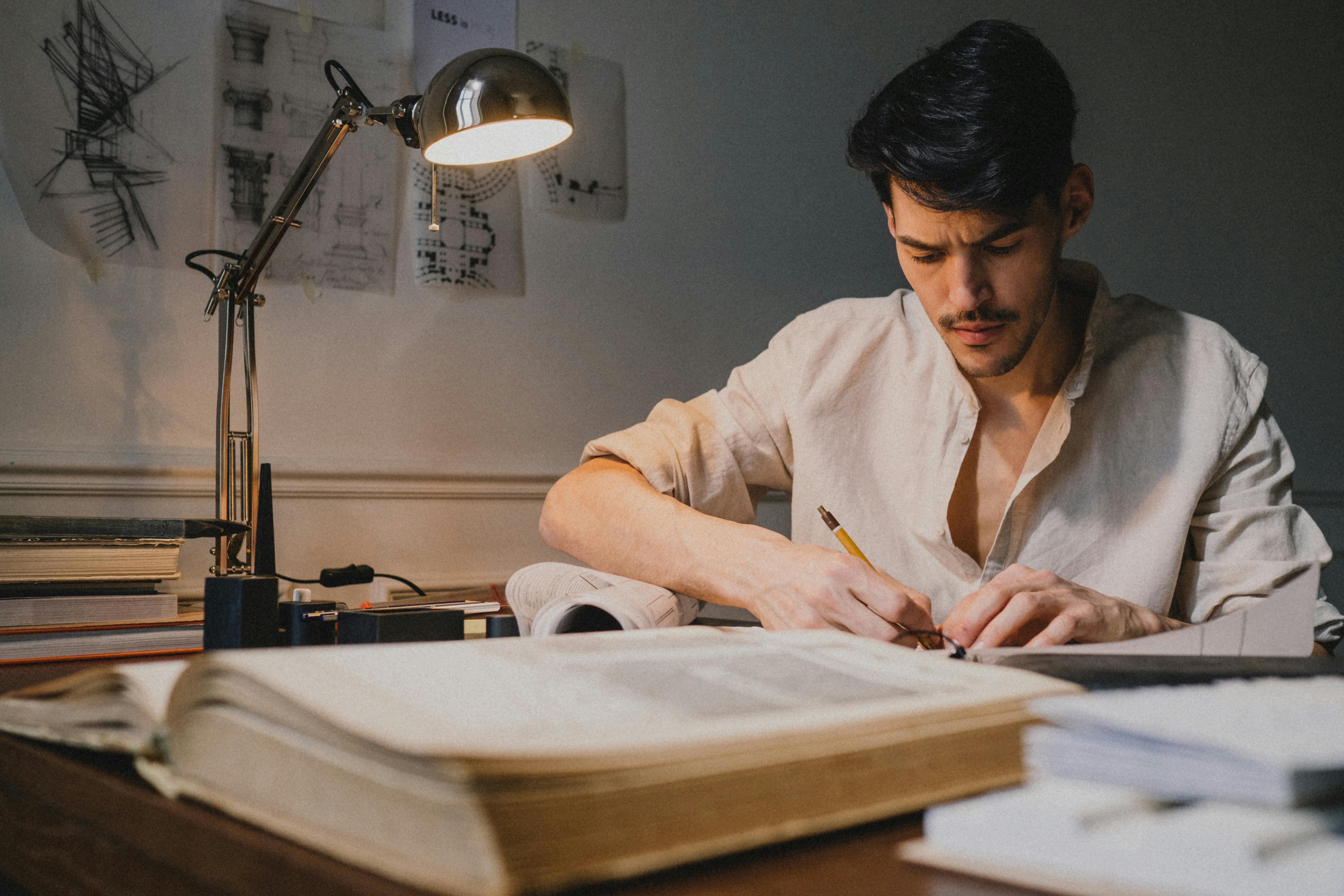 Architect deeply focused on sketching architectural plans under desk lamp lighting.