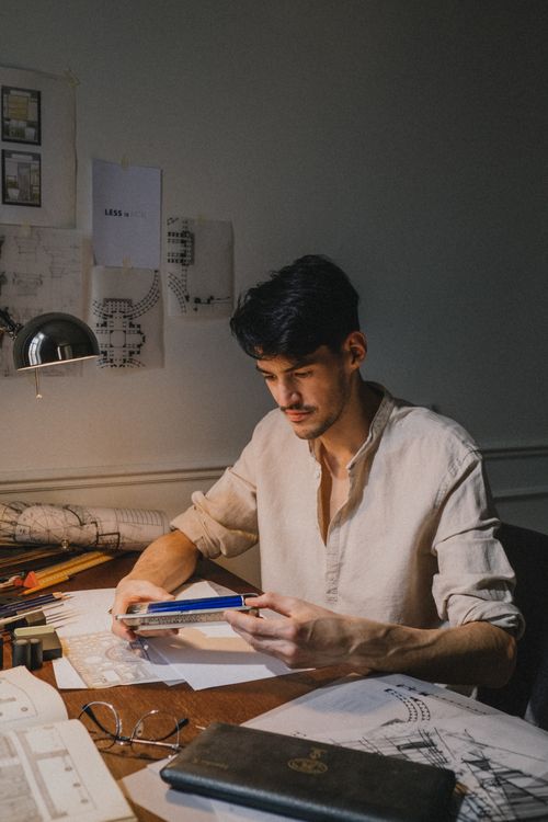 Free Architect working on designs at a desk filled with plans and sketches. Stock Photo