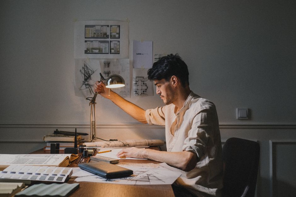 Architect working at a desk with plans and sketches in a dimly lit office setting.
