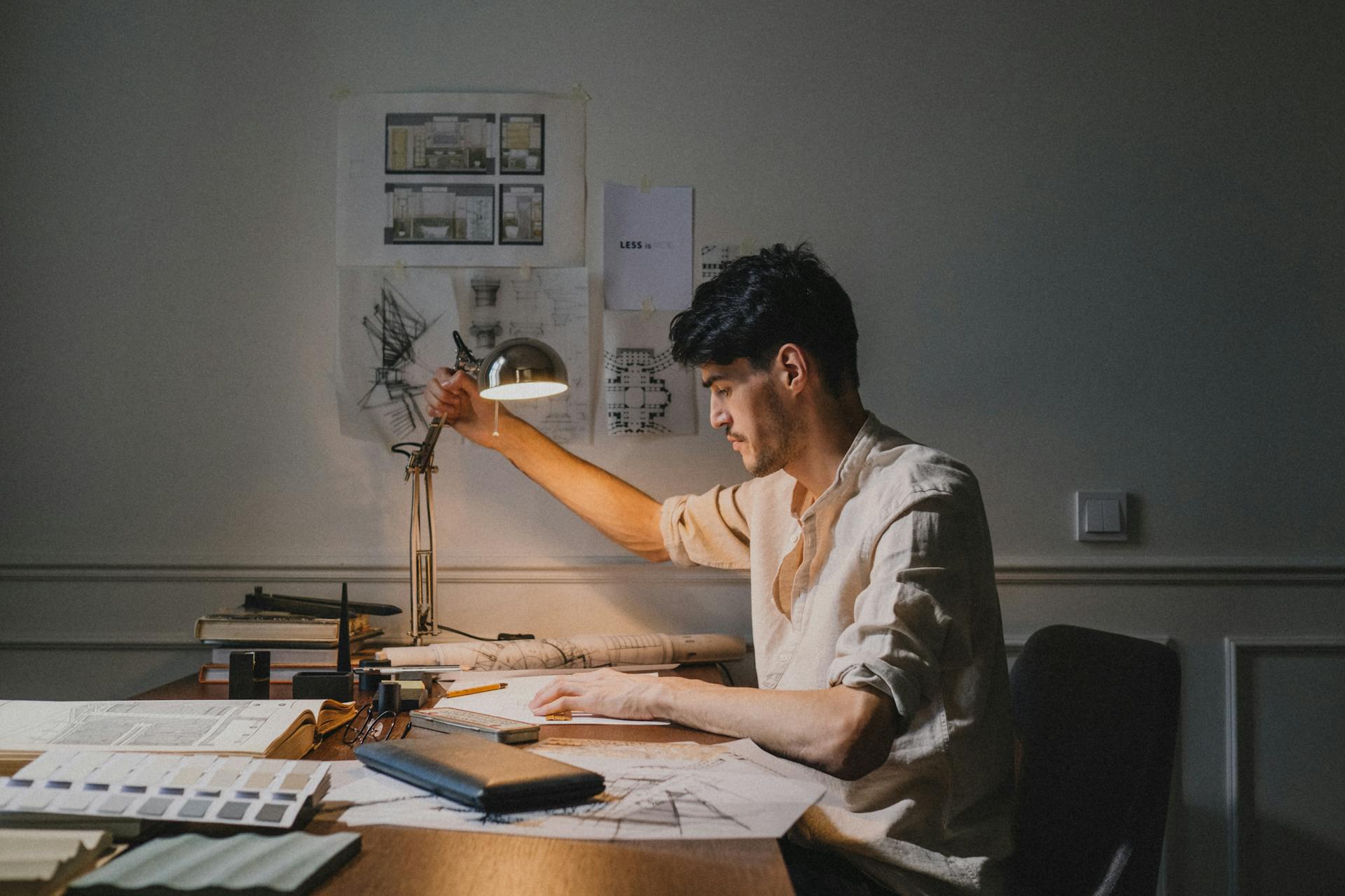 Architect working at a desk with plans and sketches in a dimly lit office setting.