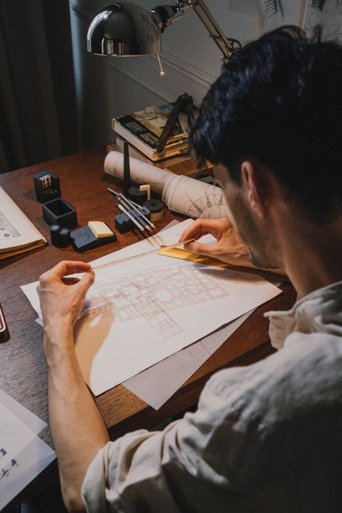 Free Man drawing architectural plans on a desk with various tools and blueprints. Stock Photo