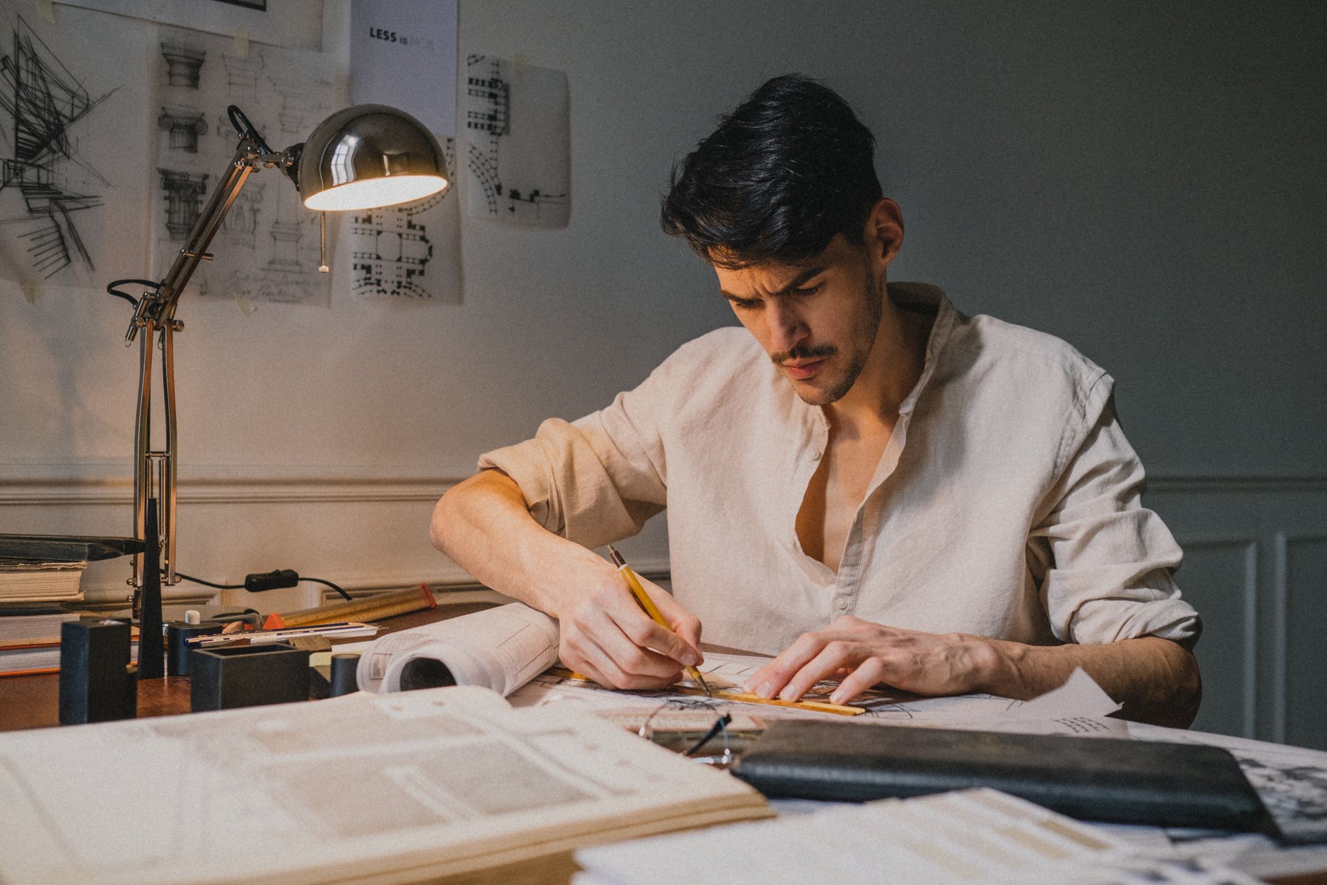 A focused architect sketching designs at a desk, illuminated by a lamp indoors.