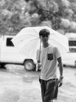 A black and white photo of a young man holding an umbrella in the rain.