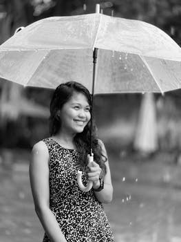 Portrait of a smiling woman holding an umbrella in the rain, captured in black and white.