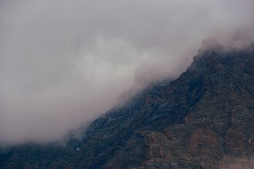Fog enveloping a rocky mountain under an overcast sky, showcasing a dramatic weather scene.