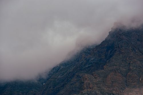 Free Fog enveloping a rocky mountain under an overcast sky, showcasing a dramatic weather scene. Stock Photo