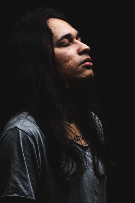 Side view portrait of a man with long hair eyes closed in a dark setting, captured in a studio.