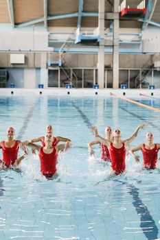 A group of women synchronized swimmers in red swimsuits perform in an indoor pool, exuding grace and precision.