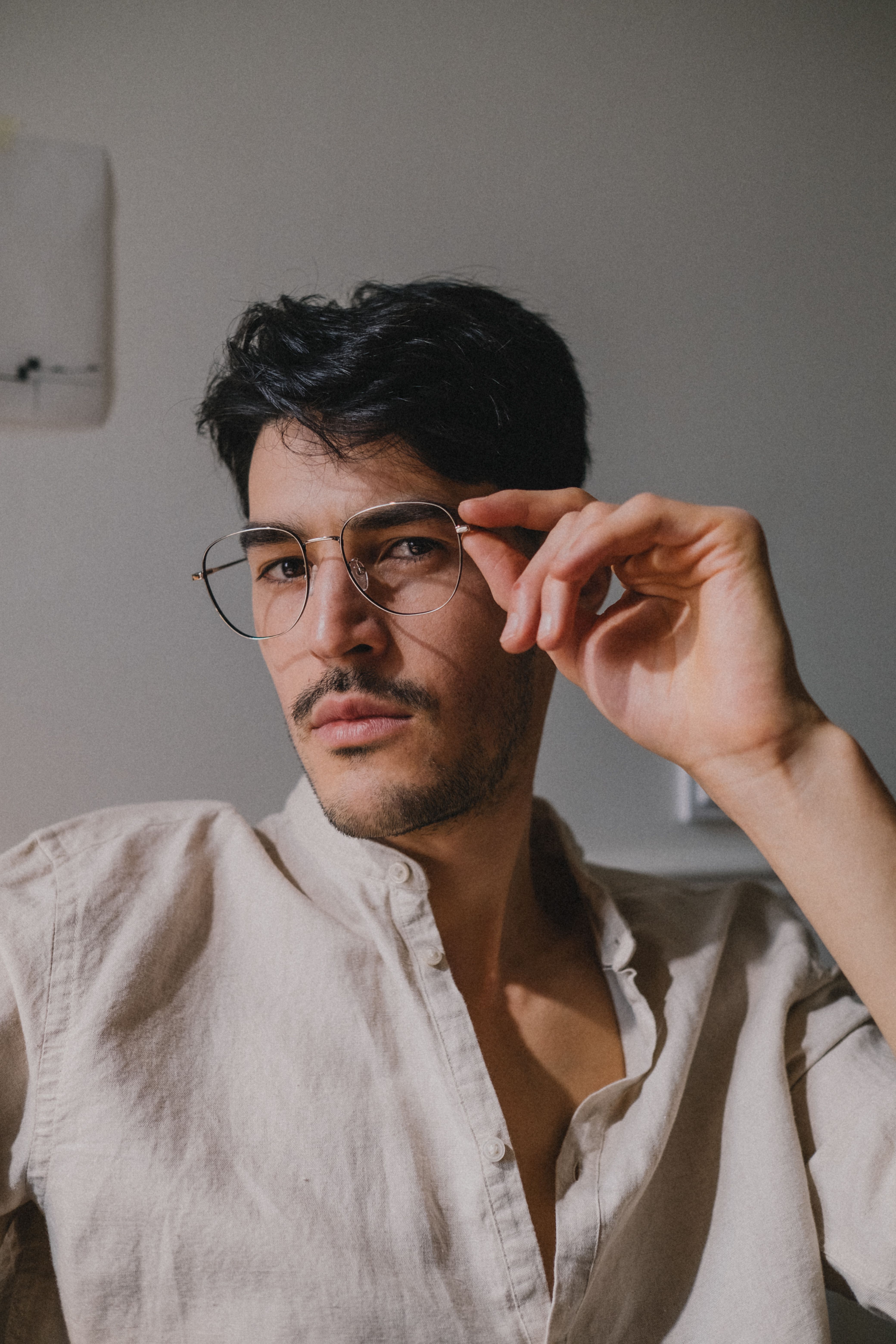 Portrait of a confident man with glasses adjusting his frame in a well-lit indoor setting.