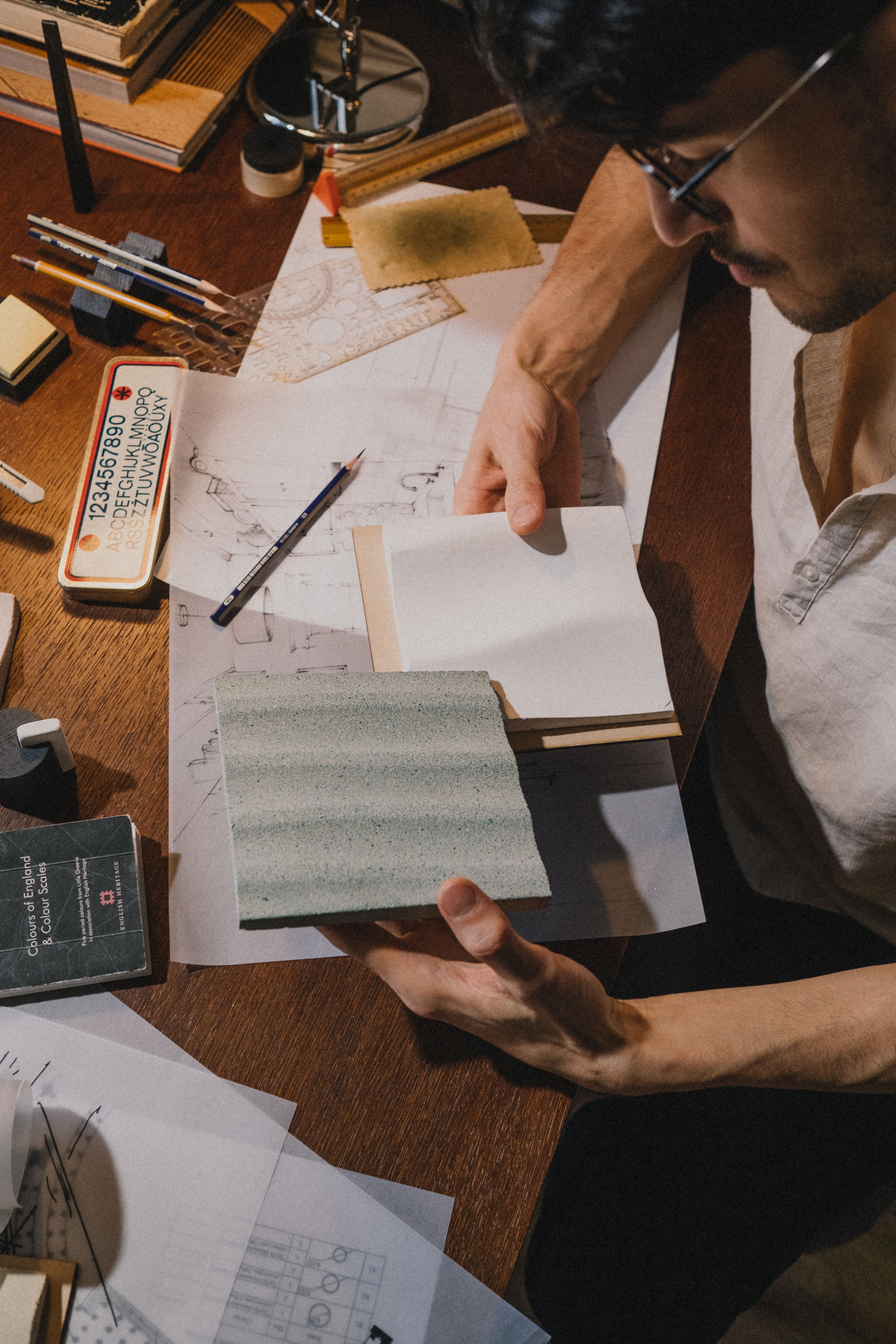 A caucasian man examining architectural designs and samples at a desk.