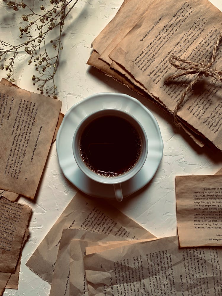 A Cup Of Coffee With Surrounded With Torn Pages Of A Book