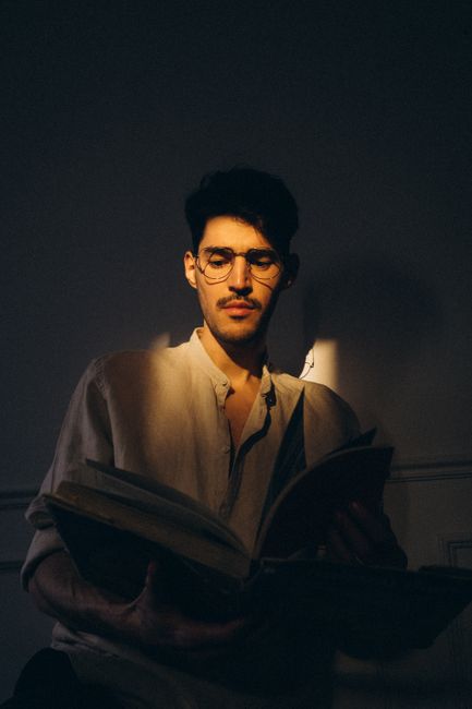 A thoughtful man reading a book indoors with soft sunlight casting shadows.