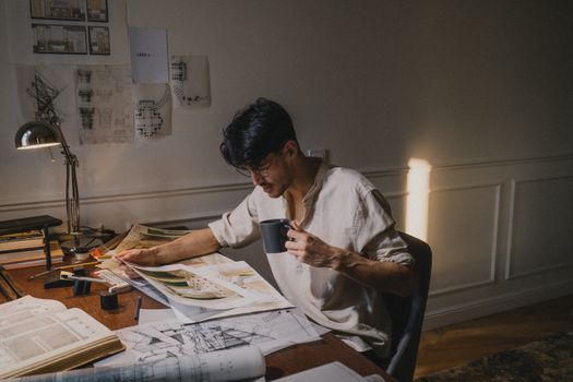 A creative architect working at home, reviewing blueprints with coffee.