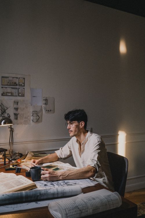 Free Architect focused on design work at a desk in a creative studio, sunlight streaming in. Stock Photo