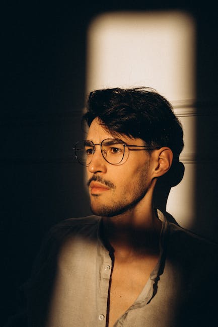 A thoughtful man with glasses captured in dramatic natural light creating a moody, introspective atmosphere.