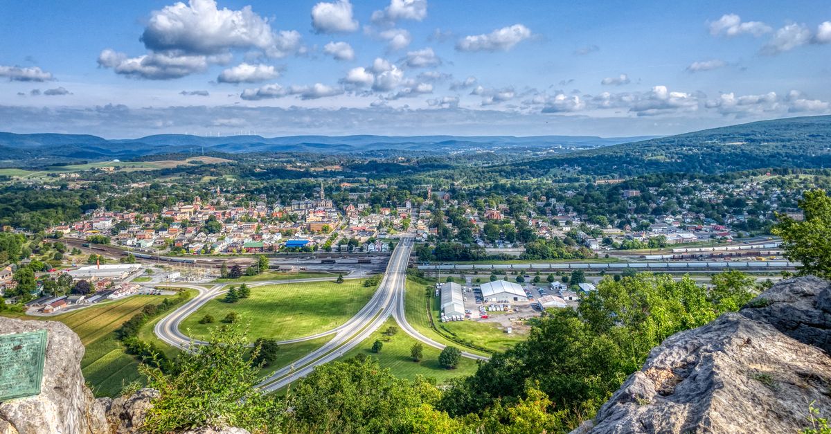 A breathtaking aerial view of Hollidaysburg, PA with rolling hills, roads, and clear blue sky.