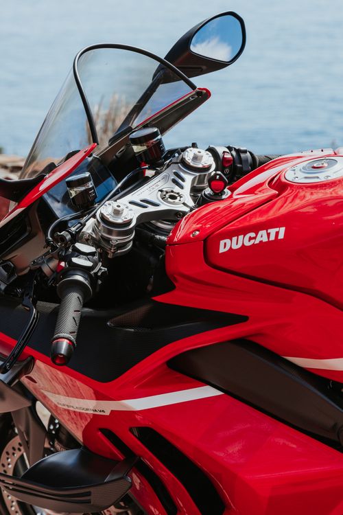Free Vibrant red motorcycle detail with ocean backdrop, showcasing sleek design and engineering. Stock Photo