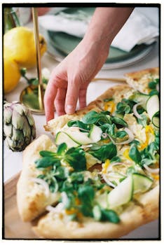 A hand reaching for a slice of gourmet vegetable pizza with fresh greens, perfect for healthy eating enthusiasts.