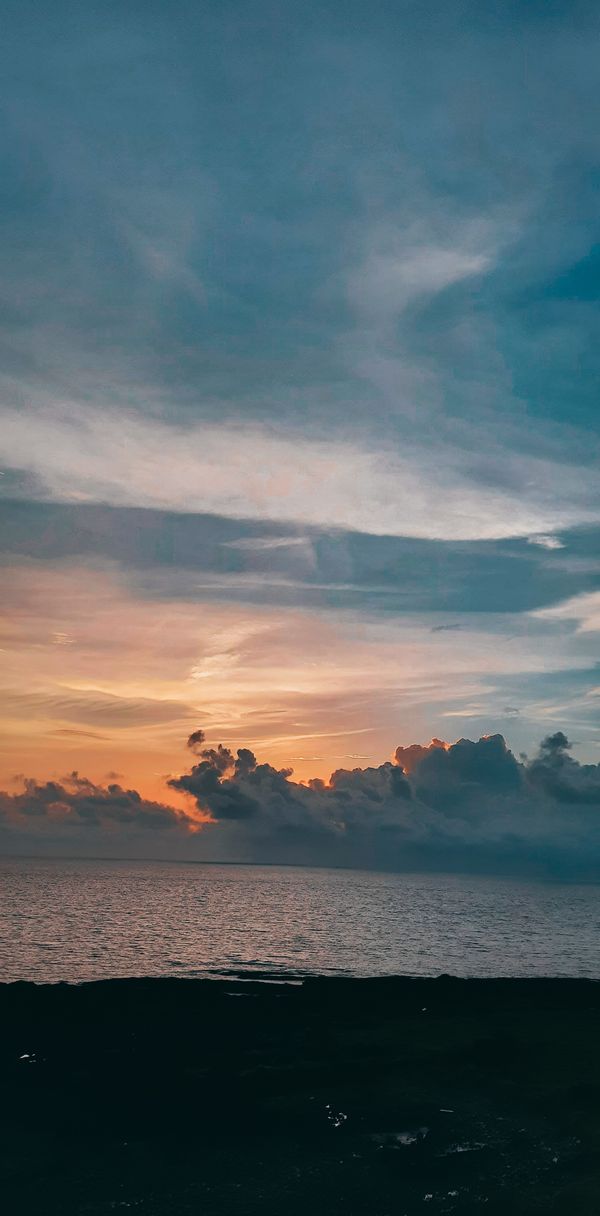 Pôr do sol tranquilo sobre o oceano com nuvens coloridas e vista serena do mar.