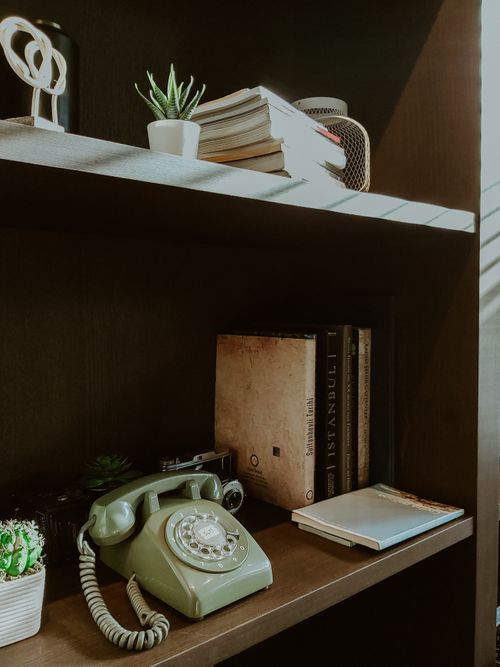 Free Shelf with vintage green rotary phone, books, and plants for a retro aesthetic. Stock Photo