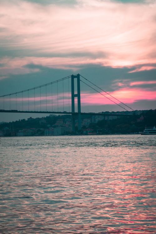 Free Dramatic sunset over a calm body of water with a silhouette of a suspension bridge. Stock Photo