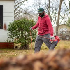 A man clearing a back garden with a handheld cordless leaf blower