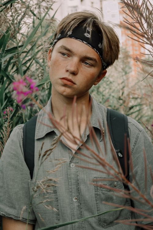 Free Teenager wearing a bandana and backpack, surrounded by nature, looking contemplative. Stock Photo