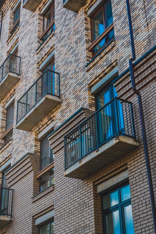 Free Low-angle view of a brick apartment building with balconies and metal railings, showcasing a modern urban design. Stock Photo
