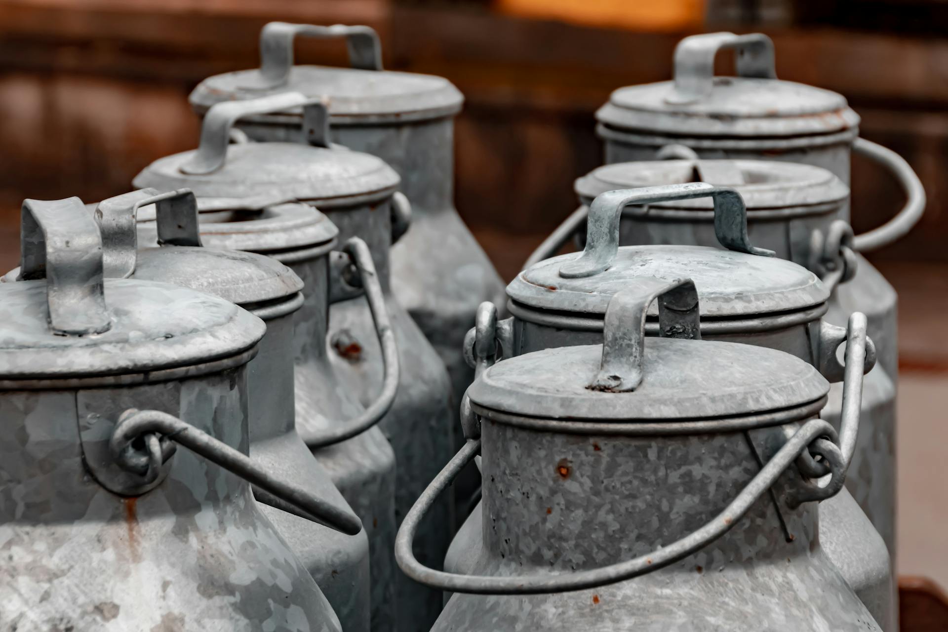 A close-up of vintage metal milk cans arranged in an outdoor rustic setting.