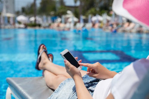 A Woman Sitting by the Poolside Using a Smartphone