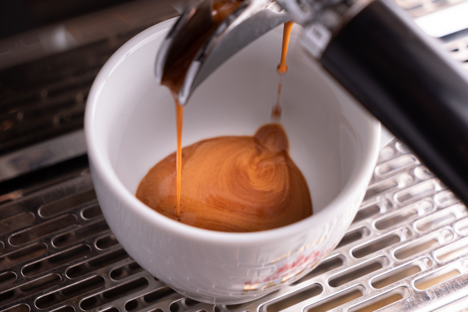 A detailed view of espresso coffee being poured into a white cup from a machine, highlighting the rich crema.