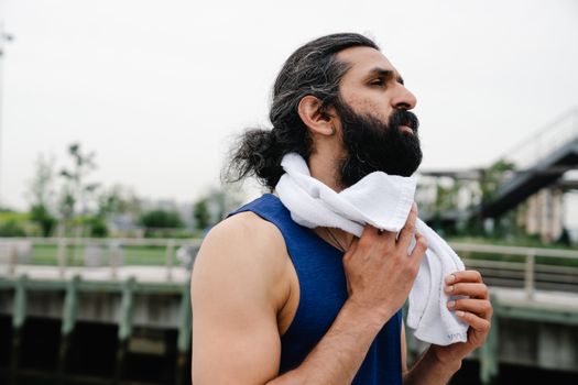 Man with a beard using a towel to cool down after an outdoor workout during the day.