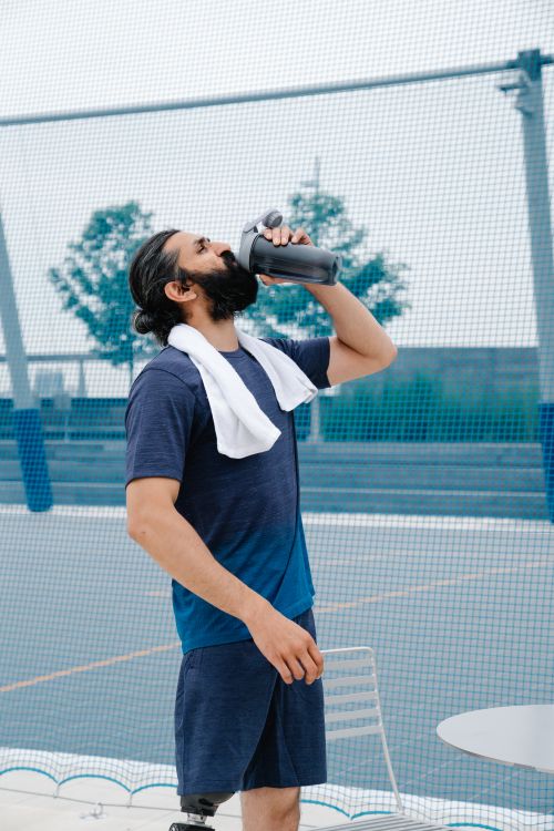 Free Man in sportswear drinking water outdoors after exercising, promoting fitness and hydration. Stock Photo