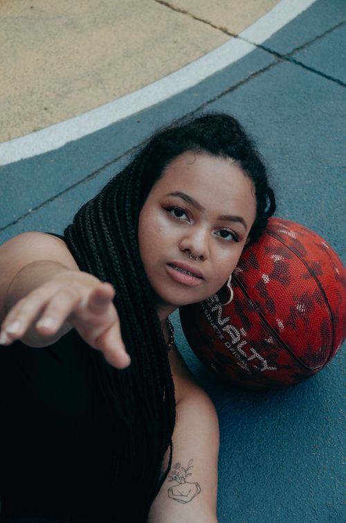 Free Young woman with braided hair lying on a court, reaching out, with a basketball beside her. Stock Photo