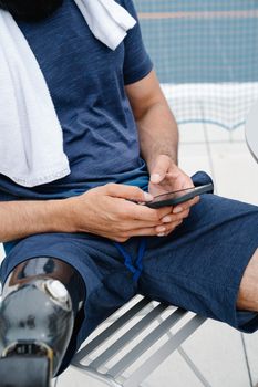 Person sitting outdoors with prosthetic leg, using smartphone, emphasizing technology and inclusivity.