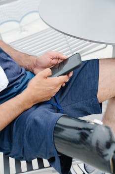 Close-up of a man using a smartphone with a prosthetic leg visible. Casual setting outdoors.